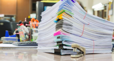 Image of examination booklets piled on a desk with colour coded corners