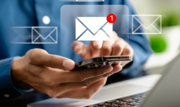 A person types on a smartphone with a laptop nearby, while a digital envelope icon—representing the digital mail room and indicating a new email notification—appears above the device.