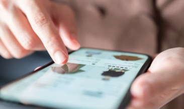 A person uses a smartphone, scrolling through an online shopping app. A finger taps images of clothing, displaying a focused and engaged interaction.