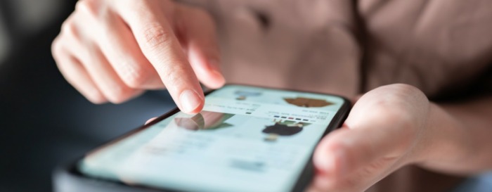 A person uses a smartphone, scrolling through an online shopping app. A finger taps images of clothing, displaying a focused and engaged interaction.